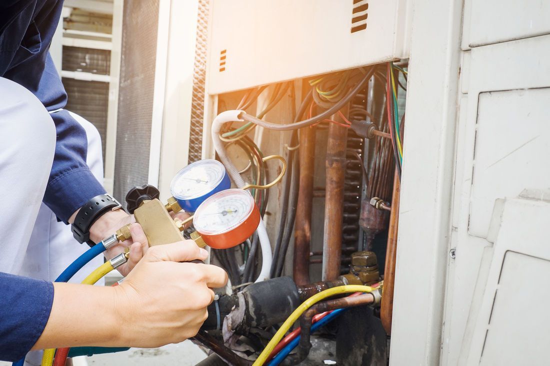 HVAC technician working on an air conditioning unit, using gauges and tools.