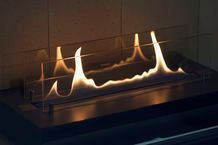 A modern fireplace with flames burning behind a glass barrier.