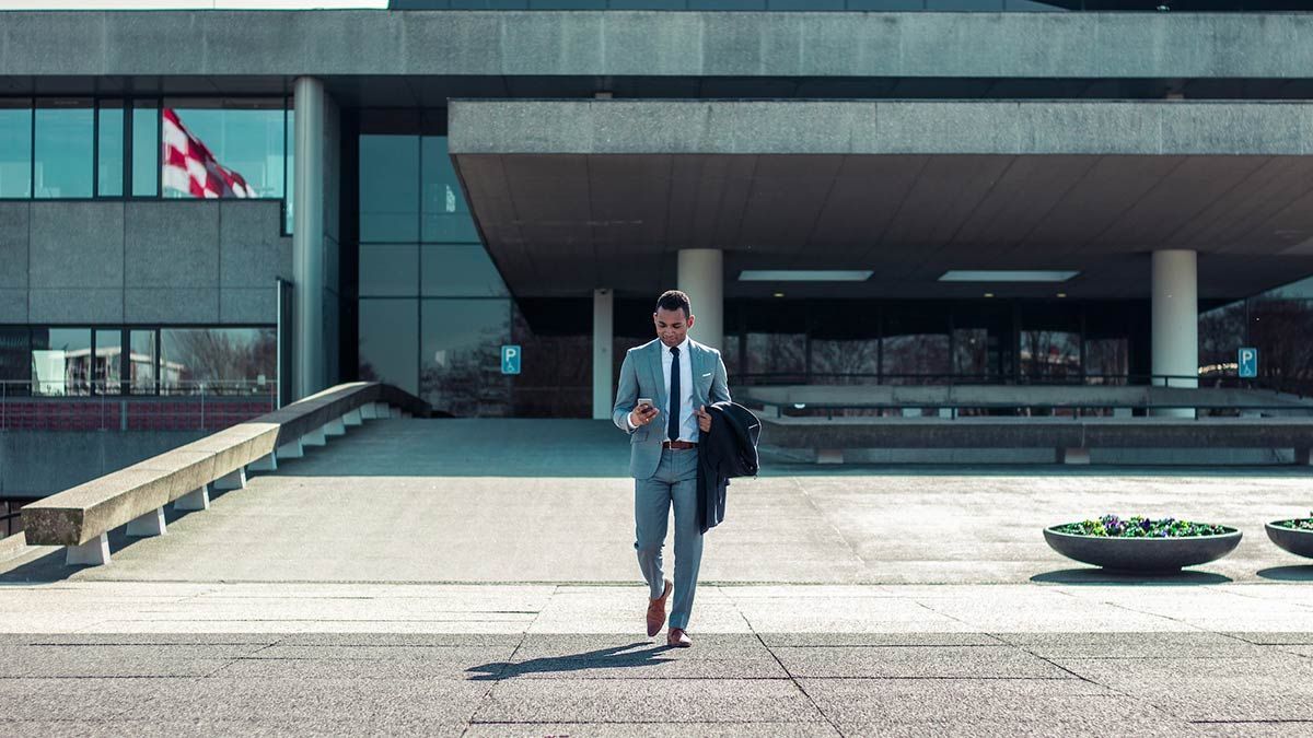 Man walking while holding black coat and phone.