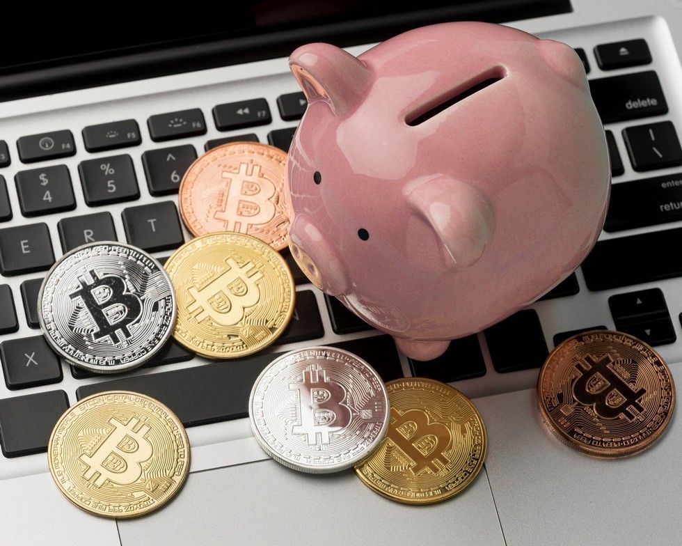 A pink piggy bank is sitting on top of a laptop keyboard surrounded by bitcoin coins.