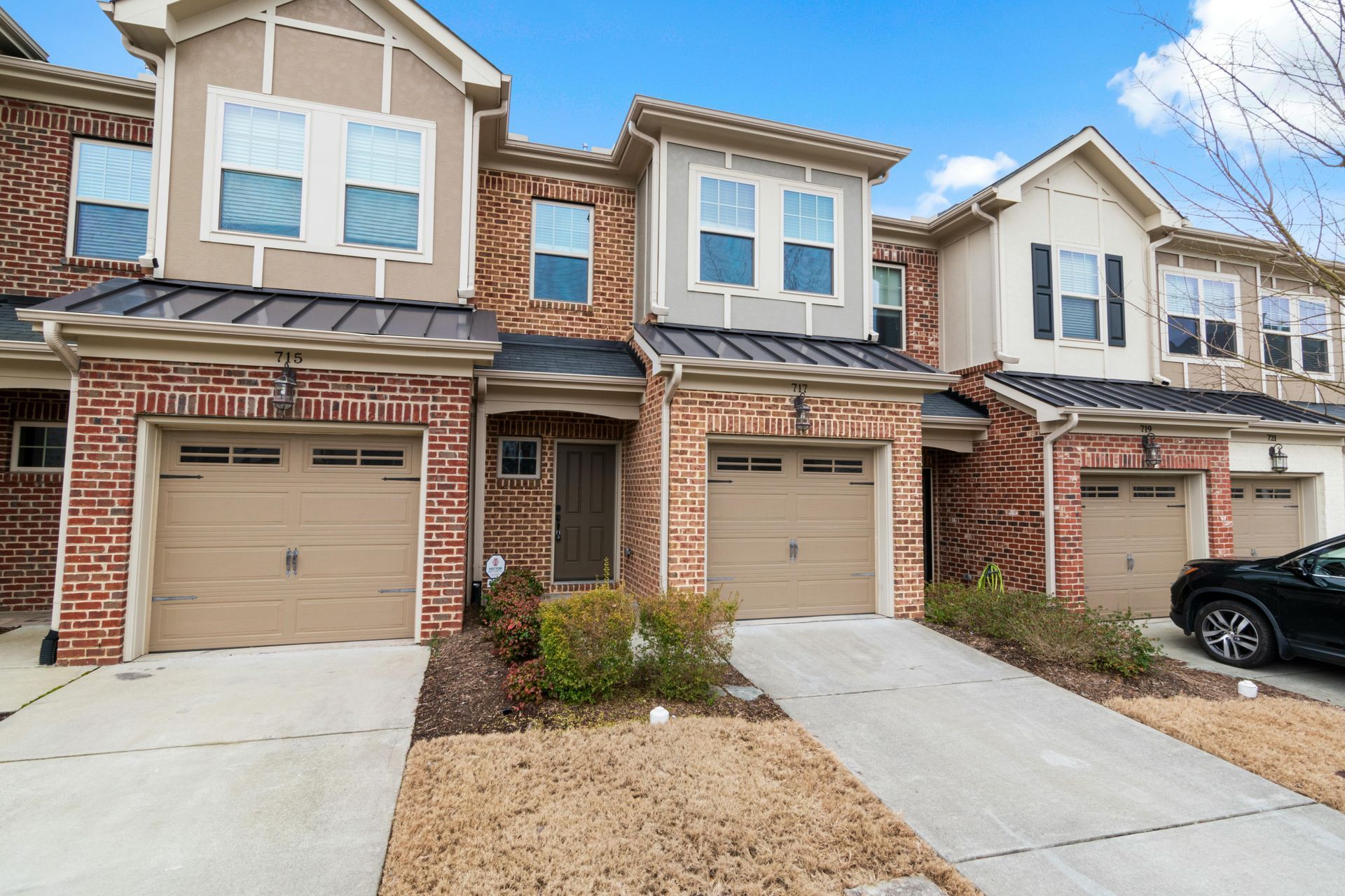Row of brick townhouses with tan garage doors and driveways under a blue sky.