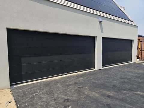 Two black garage doors in a light gray stucco building. Gravel driveway in front.
