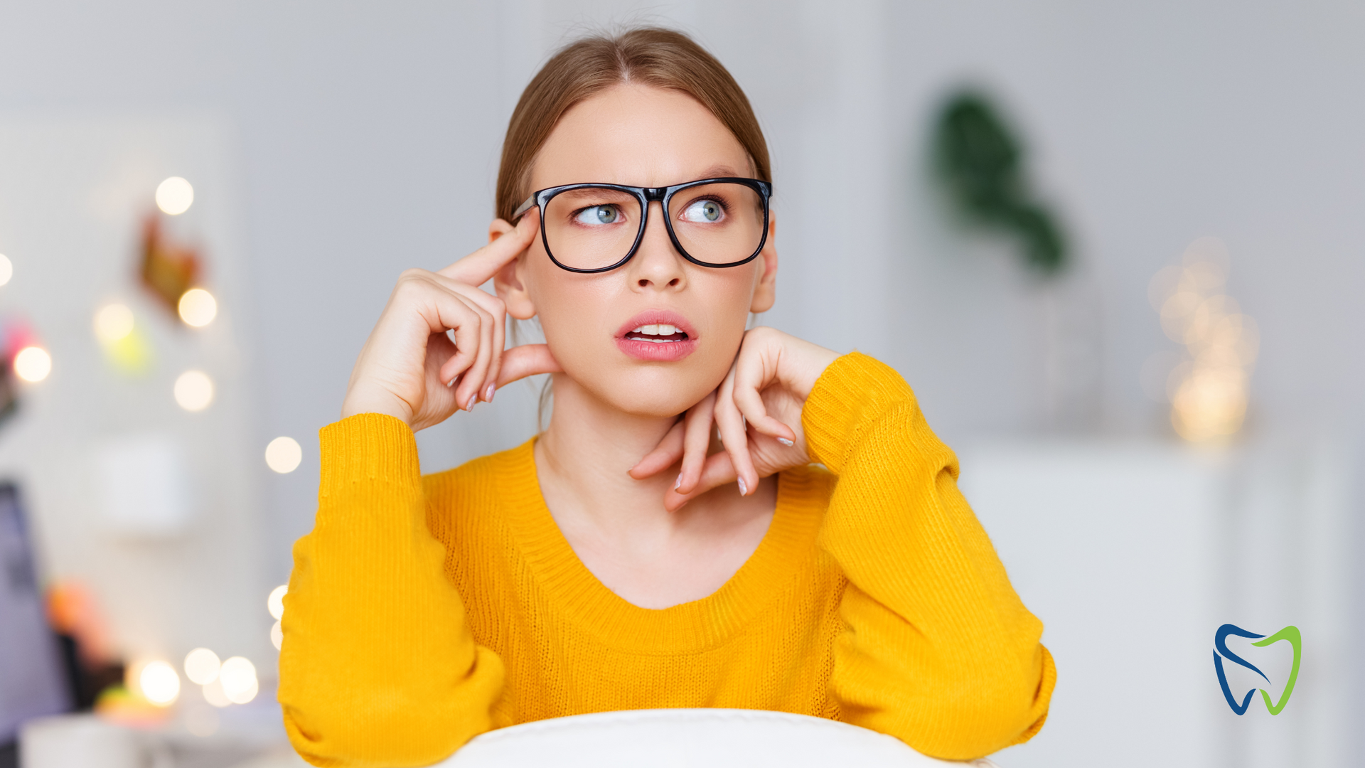 A woman wearing glasses and a yellow sweater is sitting at a table.