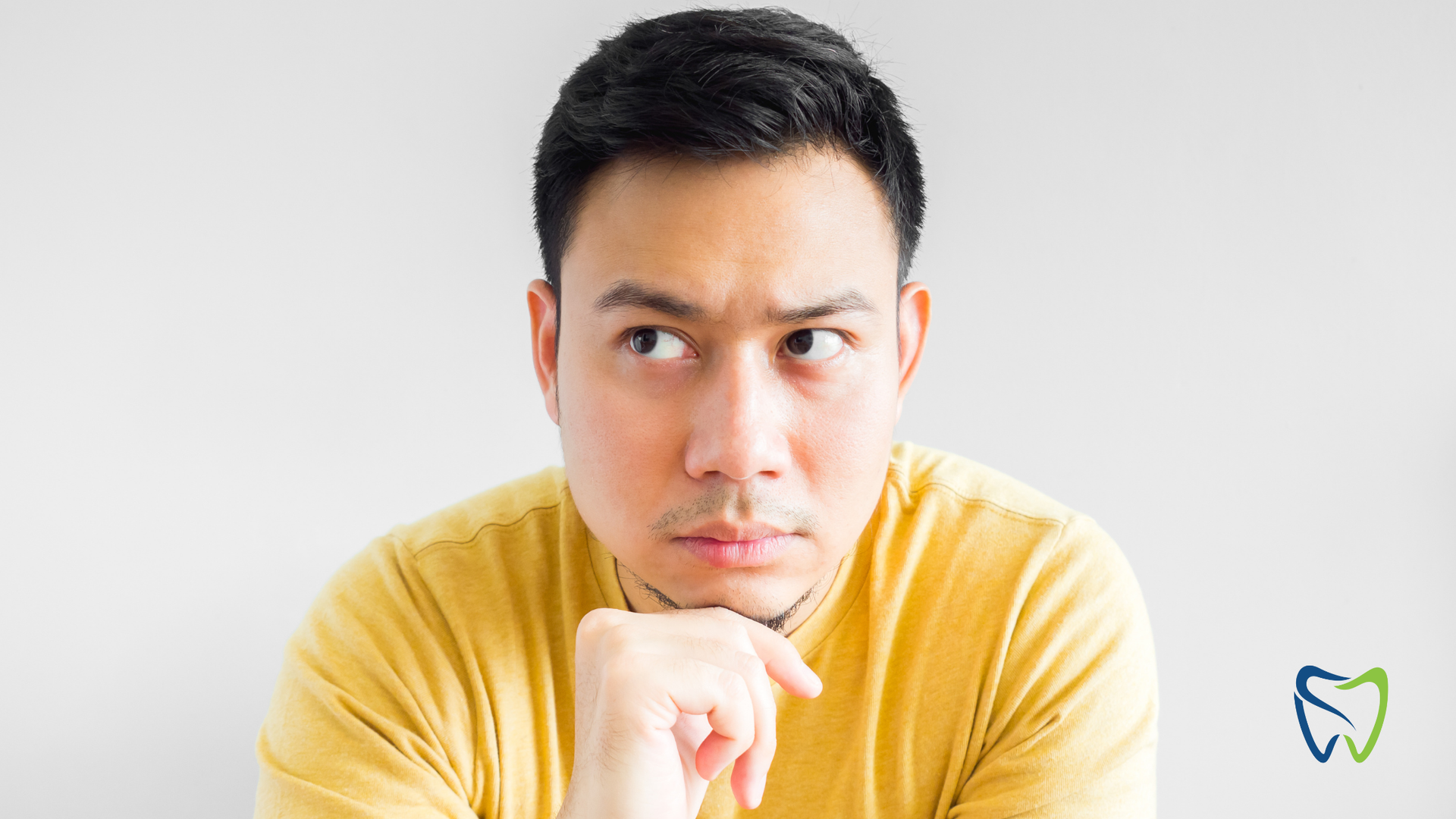 Man in yellow shirt looking thoughtful, hand on chin, against a gray backdrop.