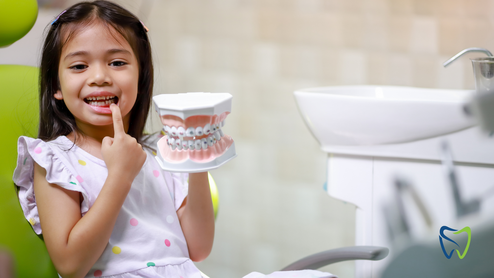 A little girl is sitting in a dental chair holding a model of her teeth.