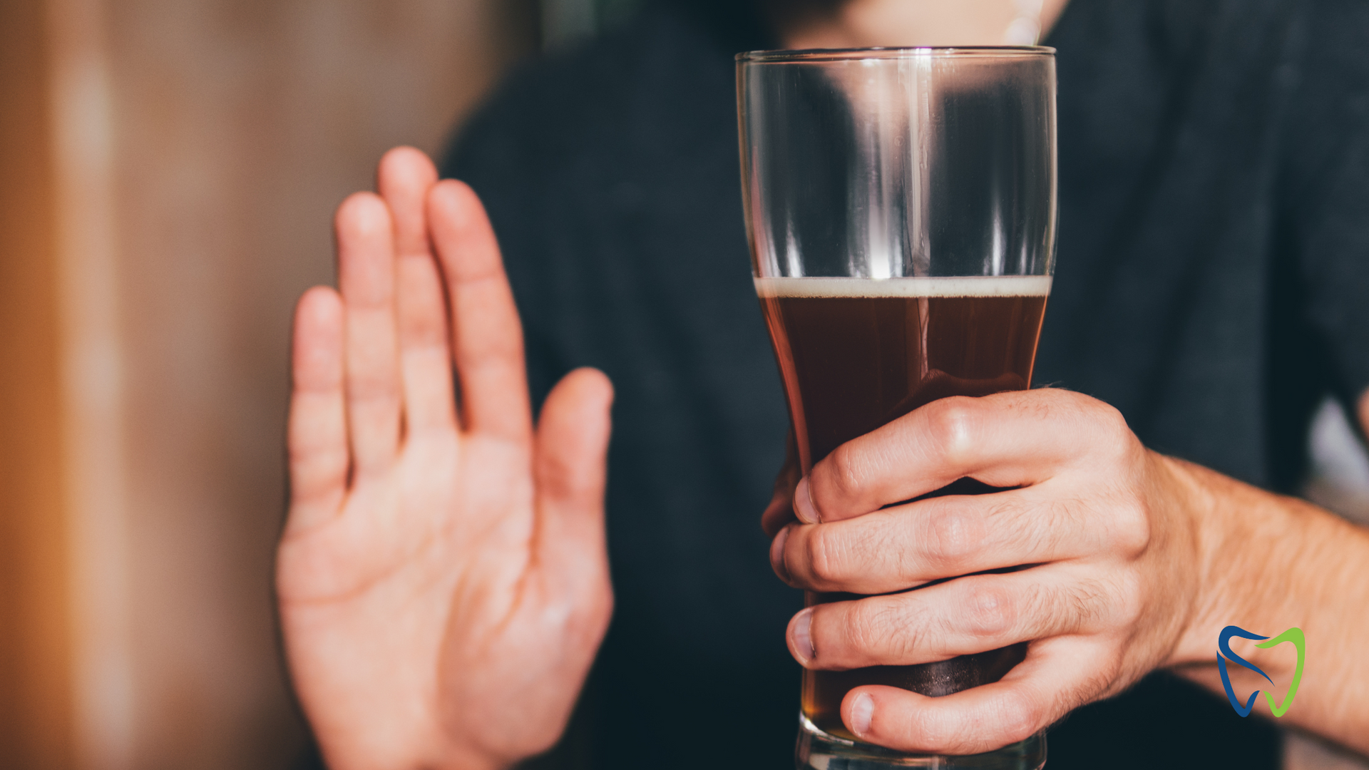 A man is holding a glass of beer and making a stop sign.