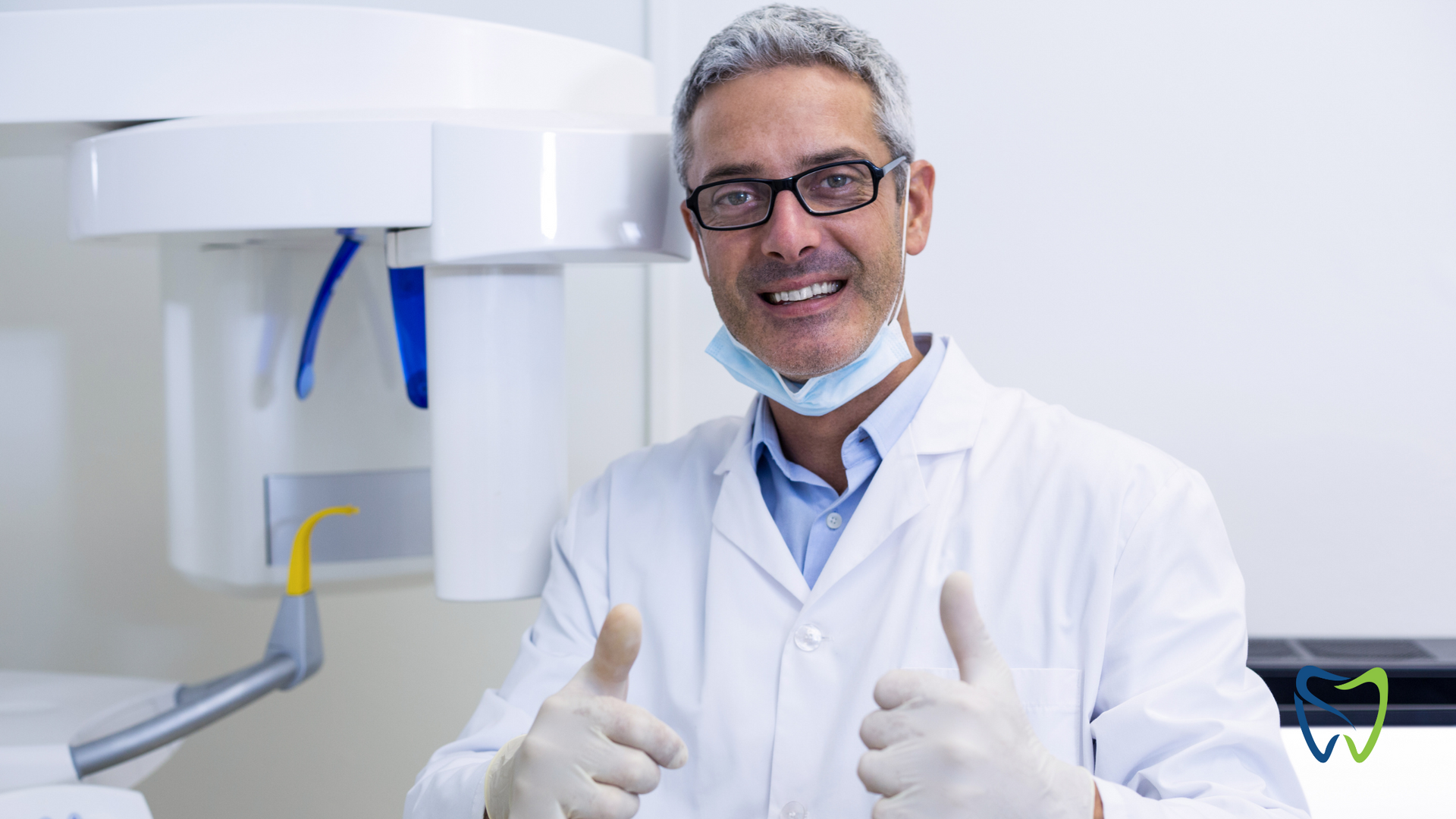 Smiling dentist in lab coat and gloves gives thumbs up in a dental office.