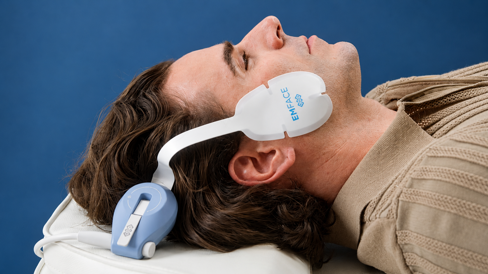 Woman receiving an EMFACE facial treatment with white head and cheek devices in a spa setting