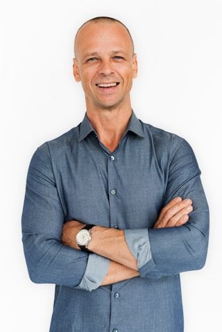 Man with crossed arms, smiling, wearing blue shirt, watch, and white background.
