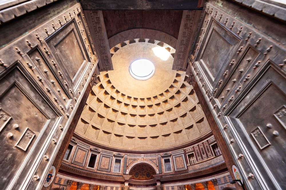 Interior view of the Pantheon, Rome, with a central oculus in the dome and large wooden doors.