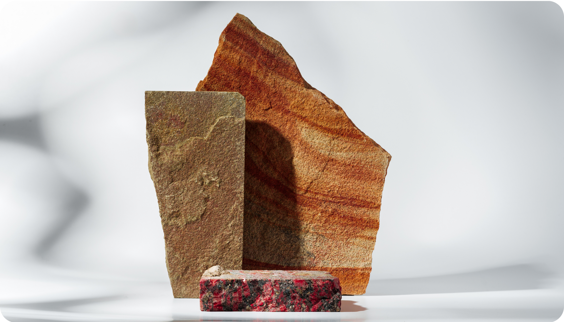 Three textured rocks: a tall brown rectangle, a layered orange triangle, and a small red rectangle.