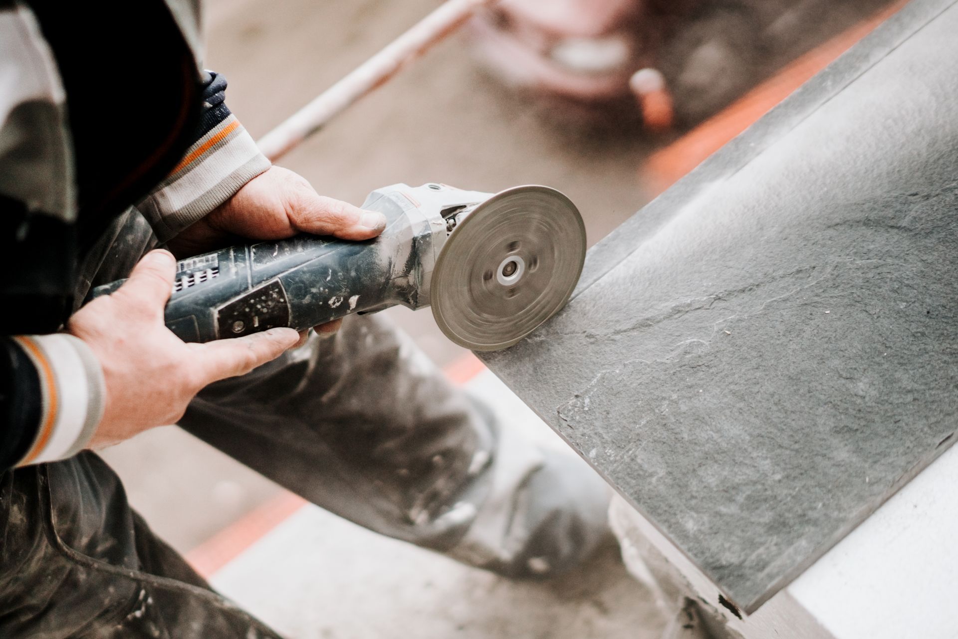 Person using a power grinder on a dark-colored stone slab, creating dust in a construction setting.