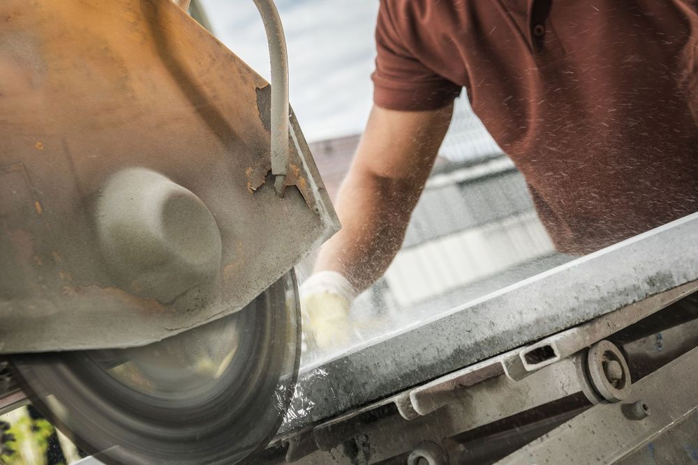 A worker cutting stone with a circular saw, generating dust; outdoors.
