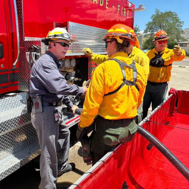 Firefighters in yellow and orange gear by a red fire truck, preparing equipment.