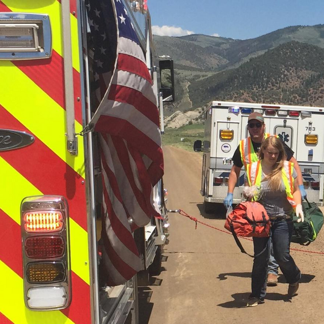Emergency responders carrying medical equipment near ambulances, American flag.