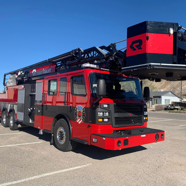 Red and black fire truck with extended ladder; outdoors on a sunny day.