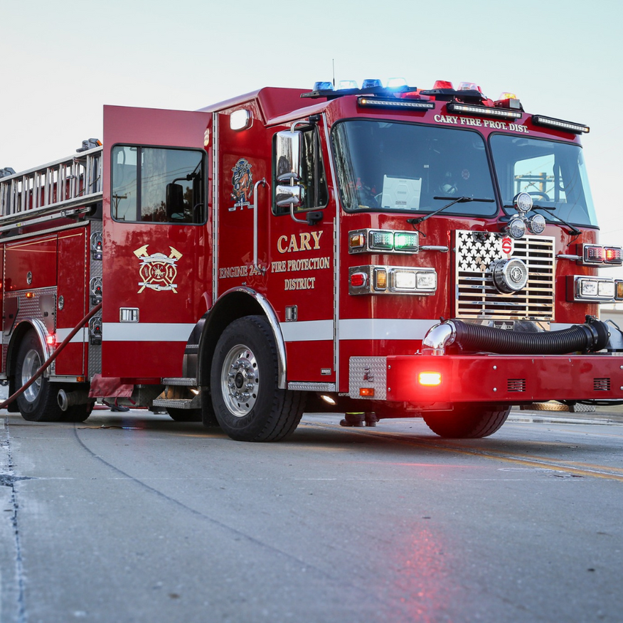 Red Cary fire truck with open door and flashing lights on a road.