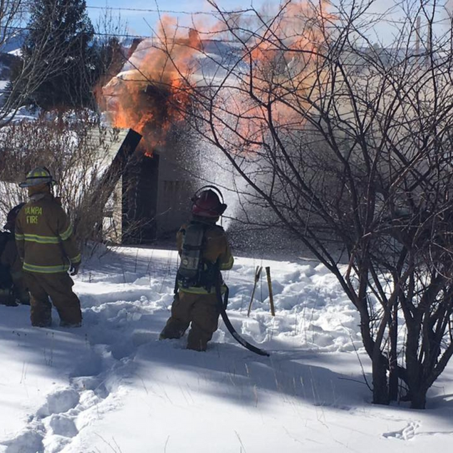 Firefighters battling a house fire in a snowy setting; flames erupt from the roof and a chimney.
