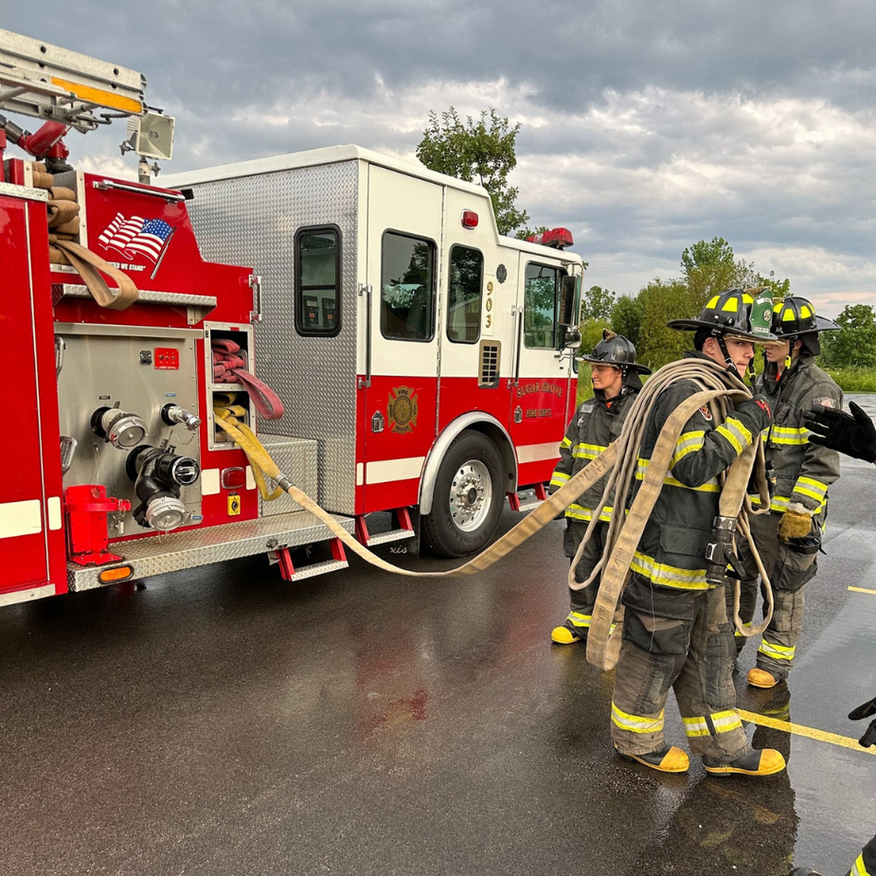 Firefighters connecting hose to a fire engine, wearing protective gear, outside.