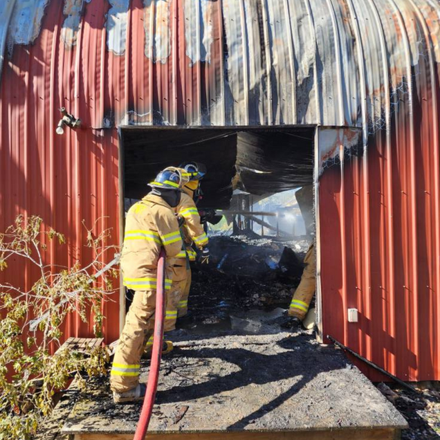 Firefighters at the entrance of a building, battling a fire. The building is red and partially burned.