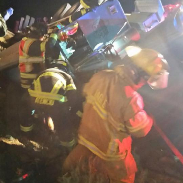 Firefighters working to extract someone from a vehicle at night. Emergency scene with lights and debris.