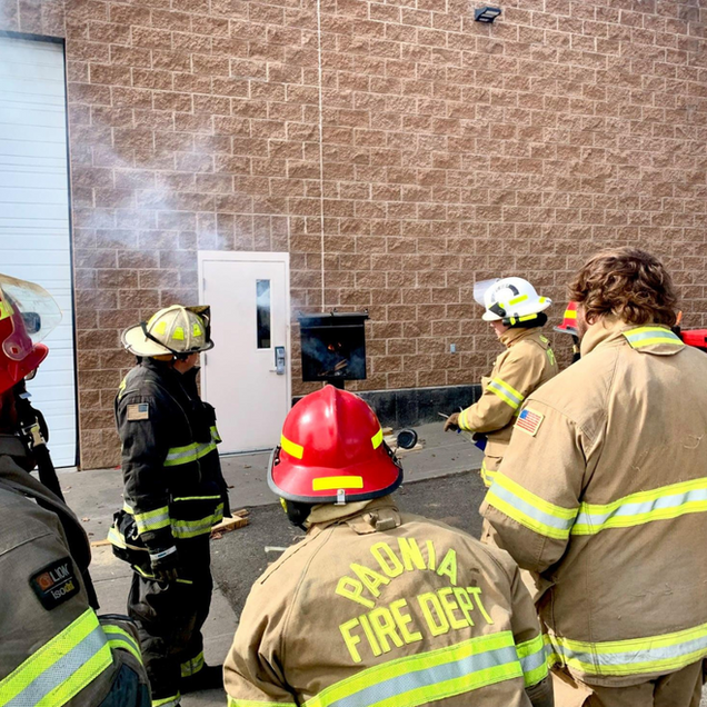 Firefighters training at a brick building with smoke billowing from a door.
