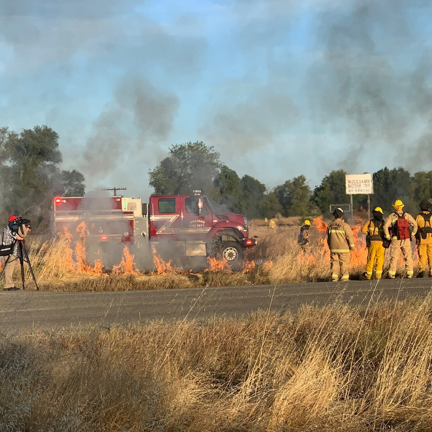 Firefighters battling a brush fire next to a red fire truck on a road.