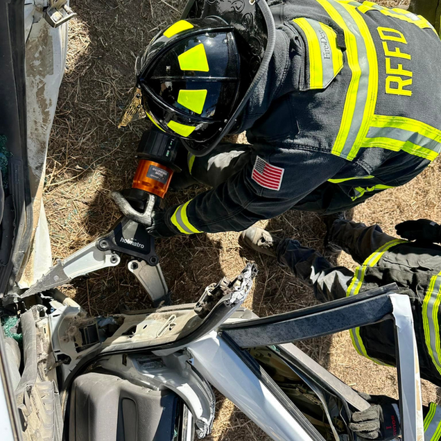 Firefighter using hydraulic rescue tools to cut open a car roof at an accident scene.