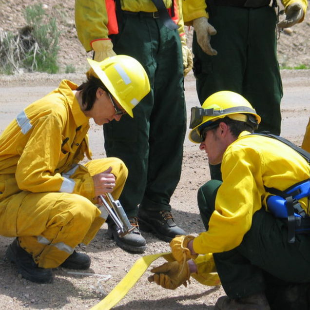 Firefighters in yellow gear connect a hose on a road.