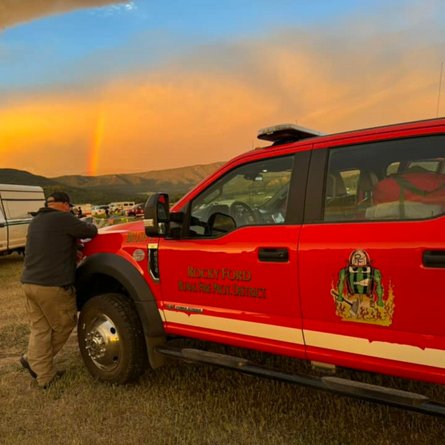 Fire truck with a person leaning on it, a rainbow in the sky. Sunset.