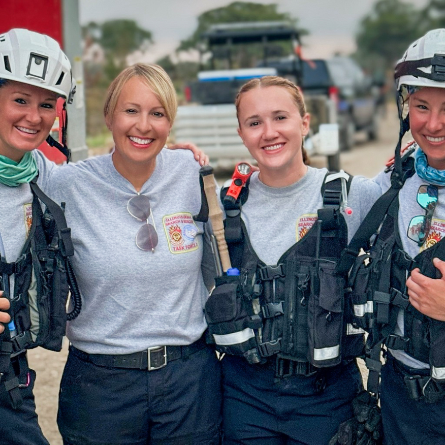 Four women in work attire with vests and helmets, smiling and posing.