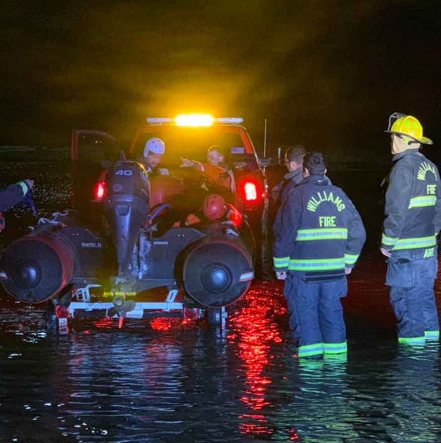 Emergency personnel around a vehicle in water at night; lights flashing.