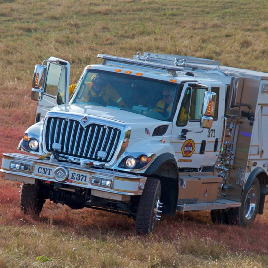 White fire truck on field; doors open. Two people in the cab.