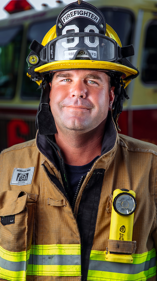 Firefighter in a tan uniform, smiling, wearing helmet with 