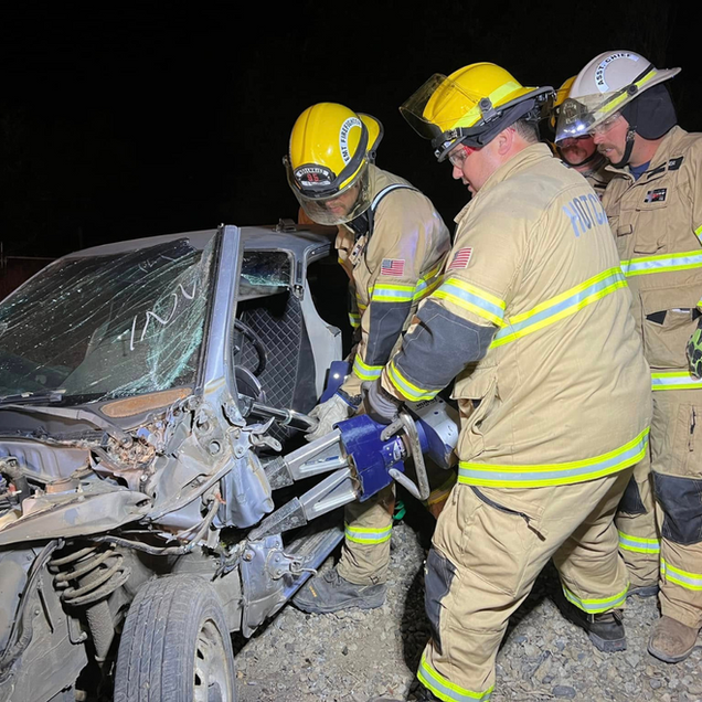 Firefighters use tools to extract a person from a damaged car at night.
