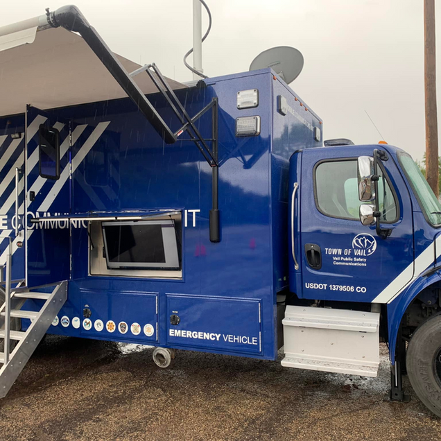 Blue emergency communications truck with antenna, satellite dish, and open awning. 