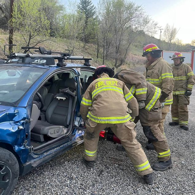 Firefighters extricate a person from a blue car after a crash.