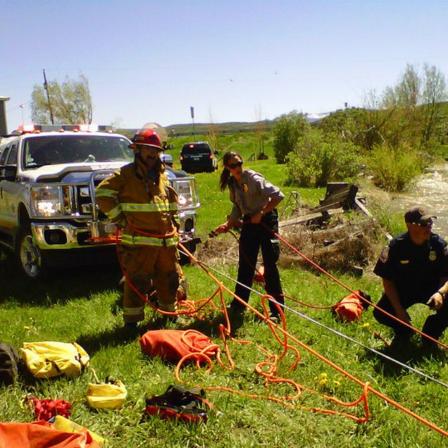 Emergency responders preparing for a water rescue; fire truck, ropes, and equipment visible.