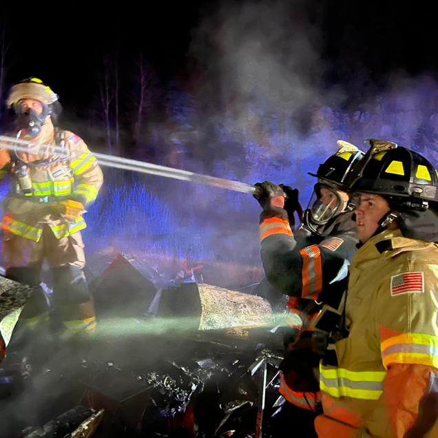 Firefighters extinguish a fire at night, spraying water onto debris and smoke.