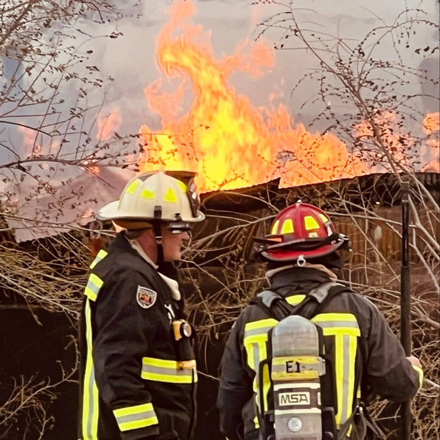 Two firefighters watching a building engulfed in flames.