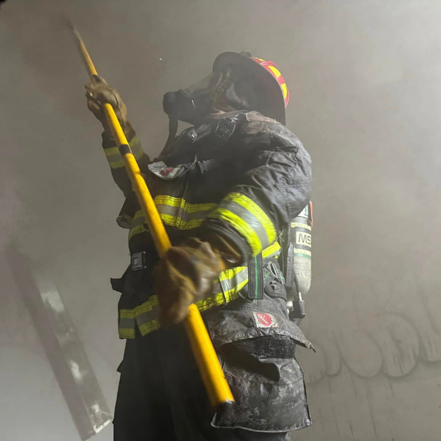 Firefighter in gear, using a tool in a smoky environment.
