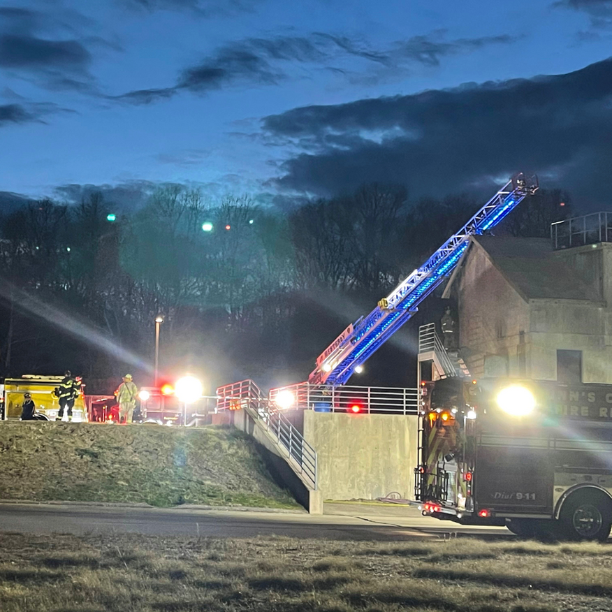 Firefighters with a ladder truck at a building at dusk, lights flashing.