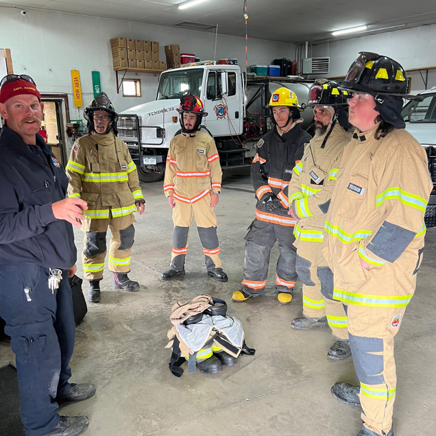 Firefighters in protective gear gather in a garage, likely for training.