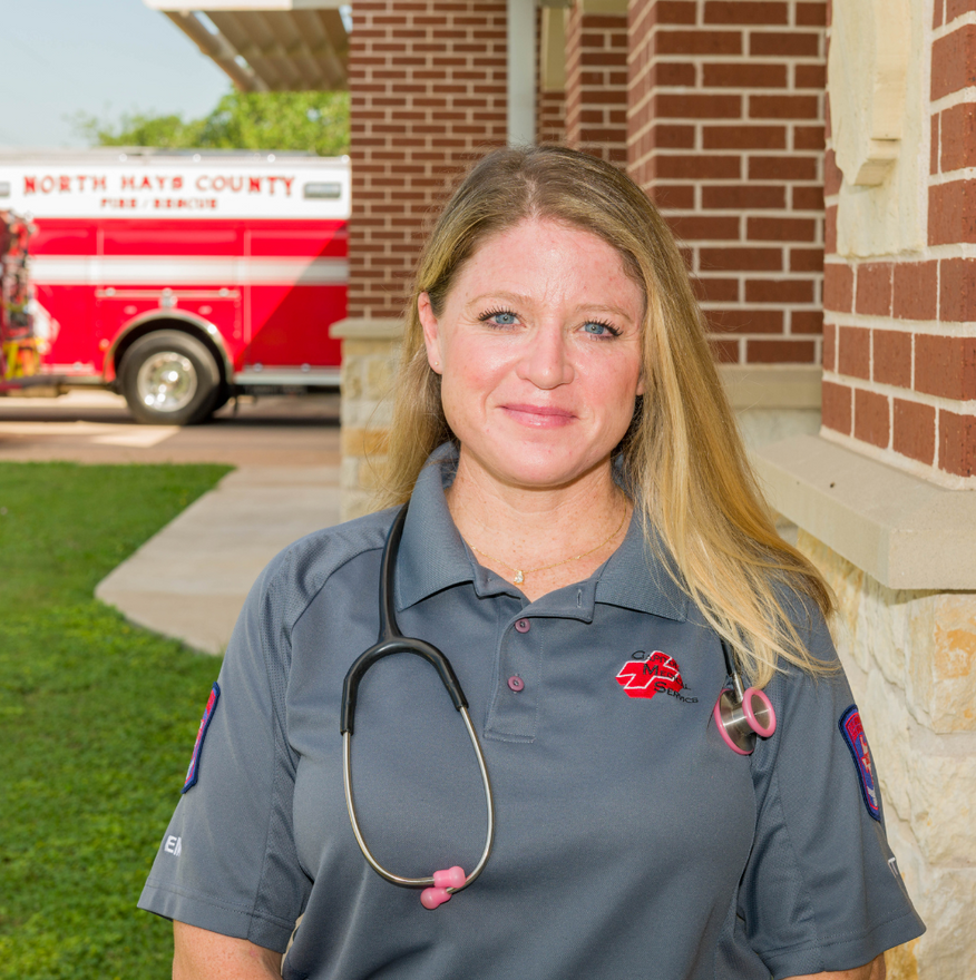 Woman in gray uniform with stethoscope in front of fire truck and building.