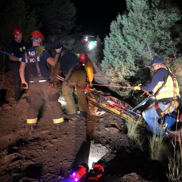 Rescue team members use ropes to carry a stretcher with a person on a dark hillside at night.