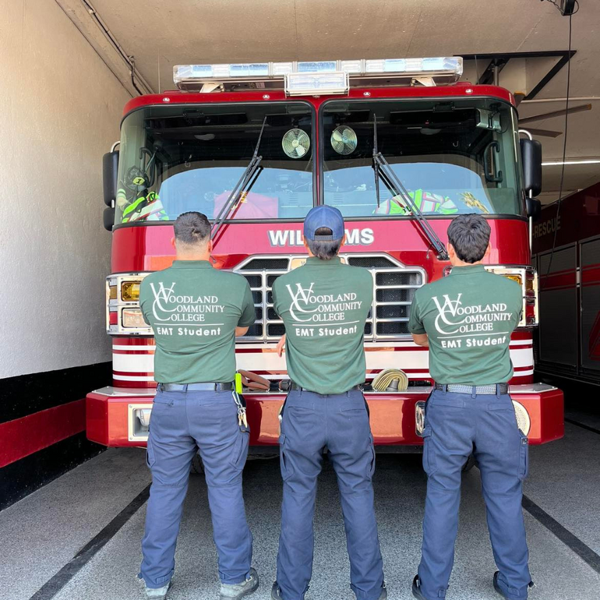 Three EMT students in green shirts pose in front of a red fire truck at Woodland Community College.