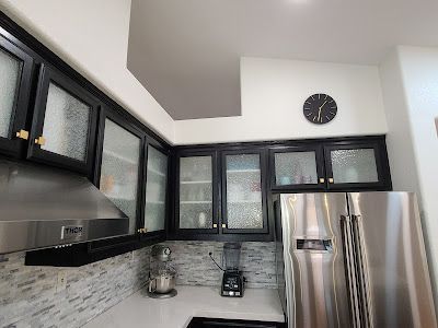 A kitchen with stainless steel appliances , black cabinets and a clock on the wall.