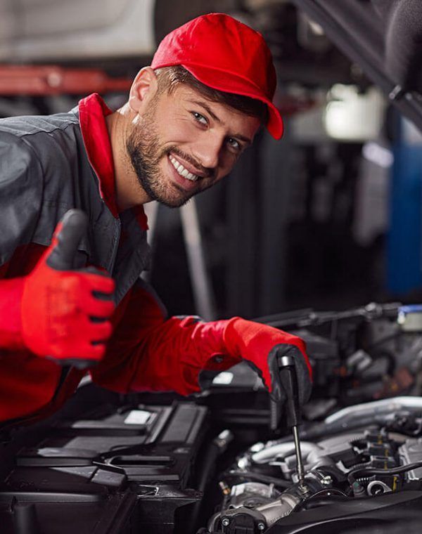 A man is working on a car engine and giving a thumbs up.