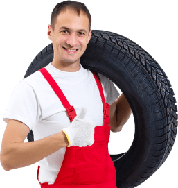 A man in red overalls is holding a tire.