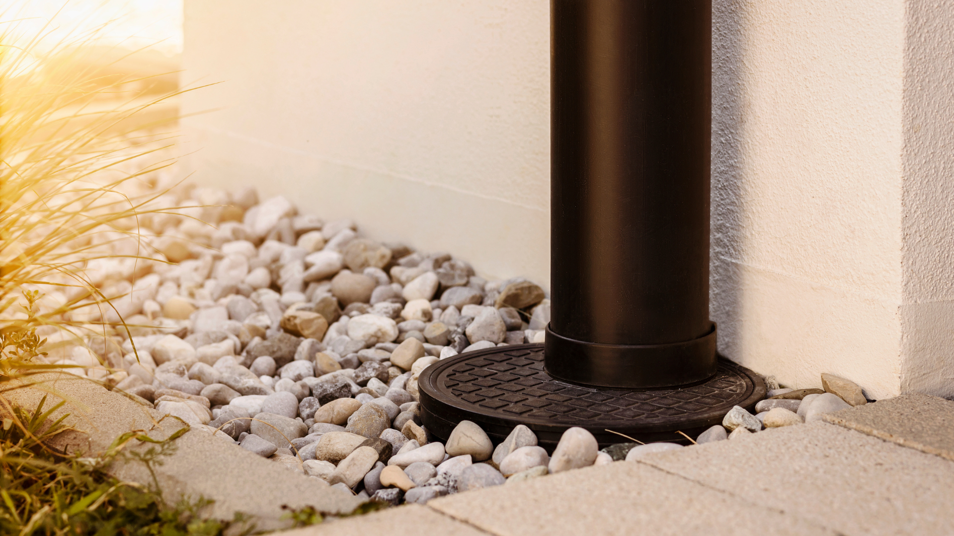 Black pole and round base surrounded by pebbles next to a light-colored wall and paving stones.